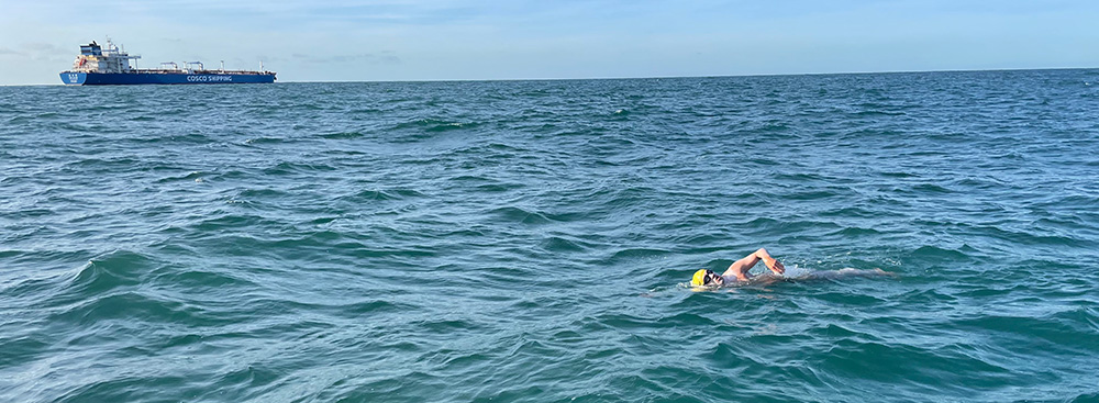 Erwan Le Roy swimming with ship in background