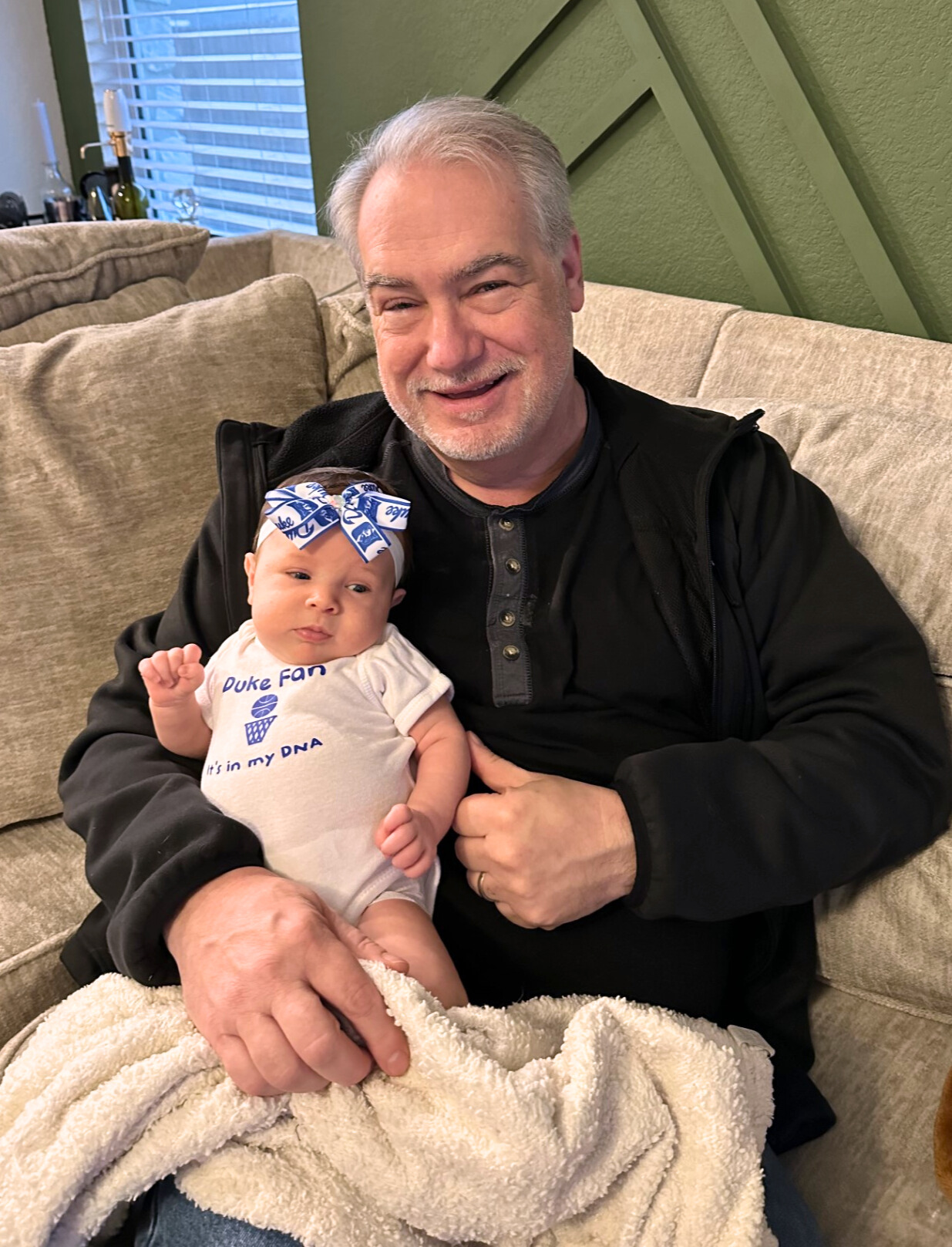 David holds his newborn granddaughter, who is wearing a Duke onesie.