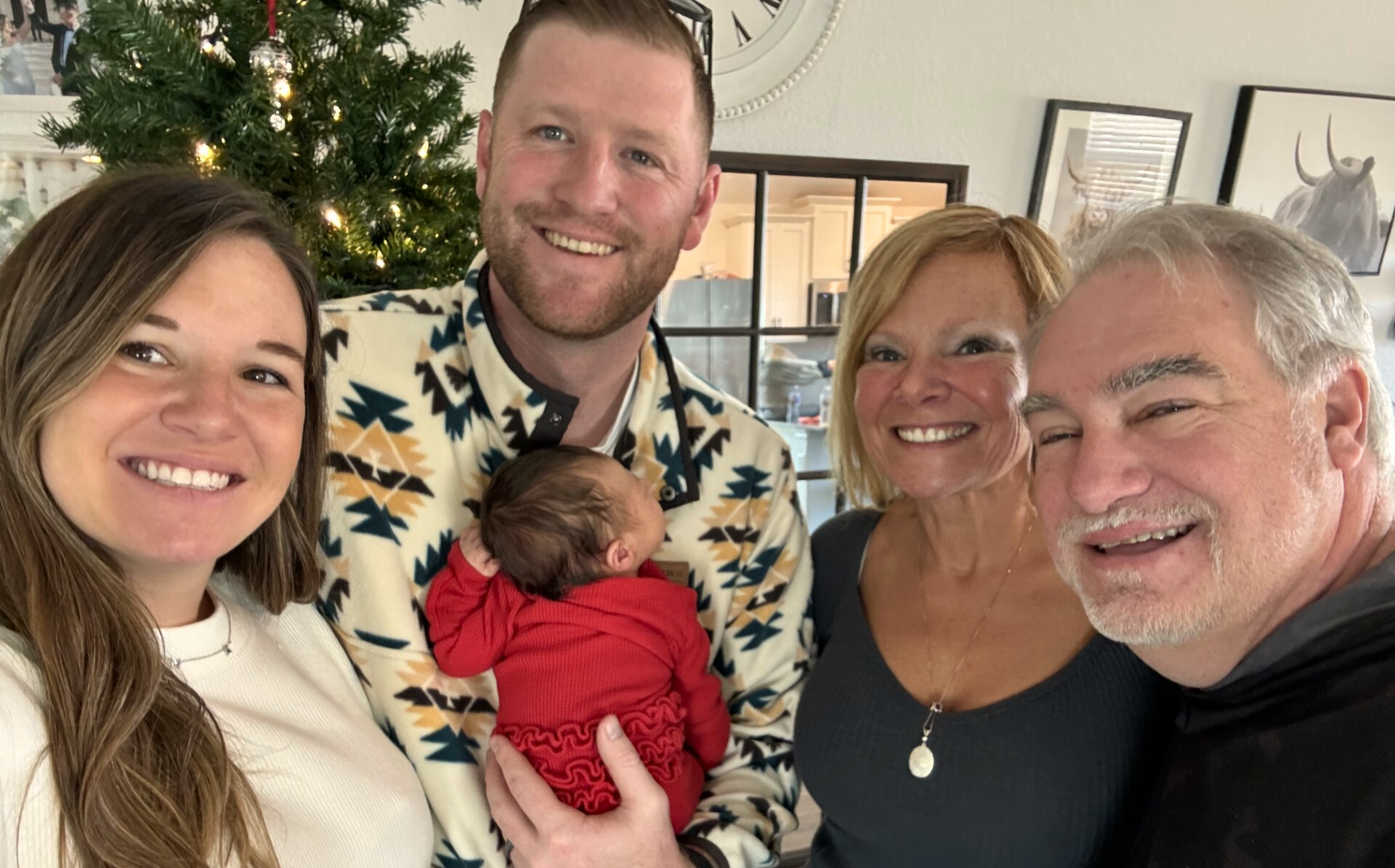 David and his family stands close together at the holidays while David's son holds his newborn against his chest.