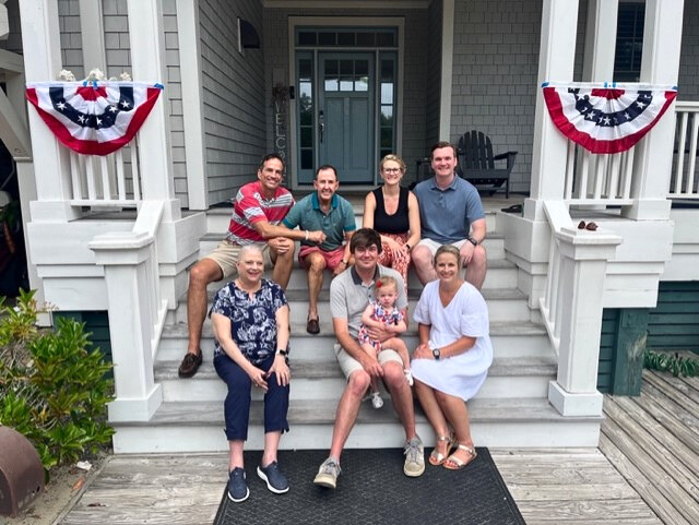 Kenneth and his family sit together on the porch of a while farm house.