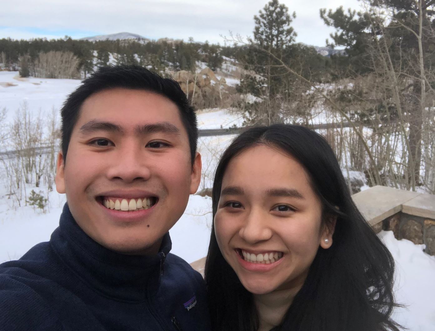 Nakhim and his wife hug while standing in front of a snowy landscape.